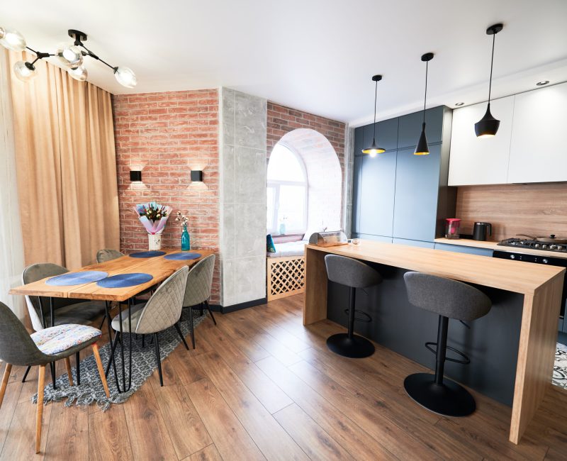 Living room and kitchen studio in dark blue color with modern furniture table, chair and stylish lamps. Concept of stylish modern interior kitchen with bar table.