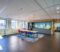 The interior of the kitchen area of a modern office with a long wooden table and chairs